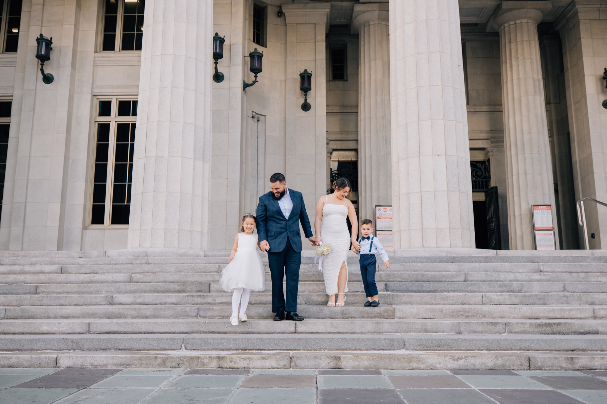 Newlywed couple descending courthouse steps hand in hand with their two young children