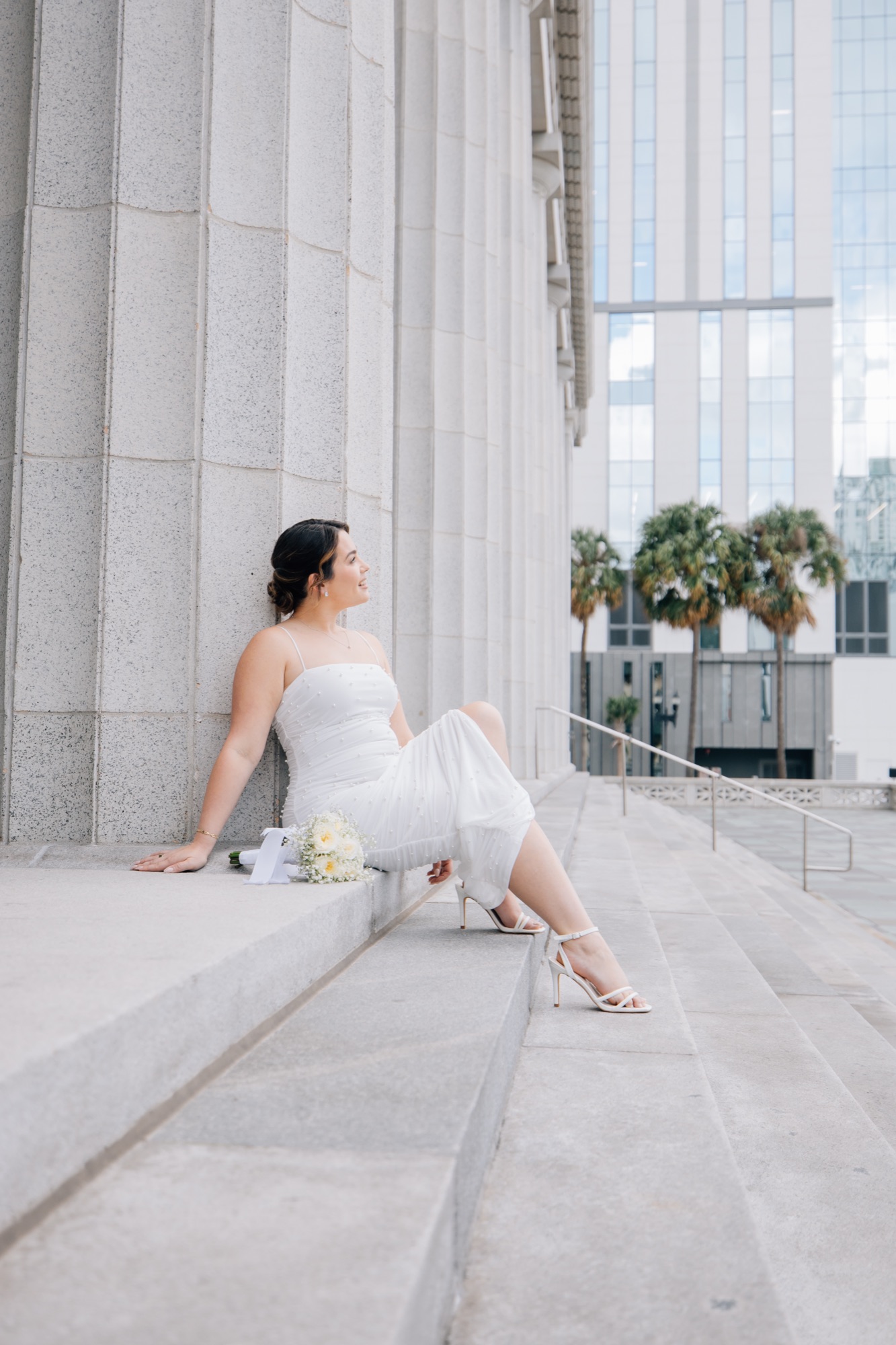 Bride in a pearl-dotted slip dress seated on the courthouse steps with her bouquet