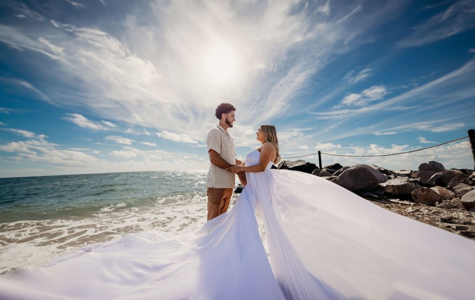 Bride's gown billowing in the ocean breeze as the couple embraces the sun
