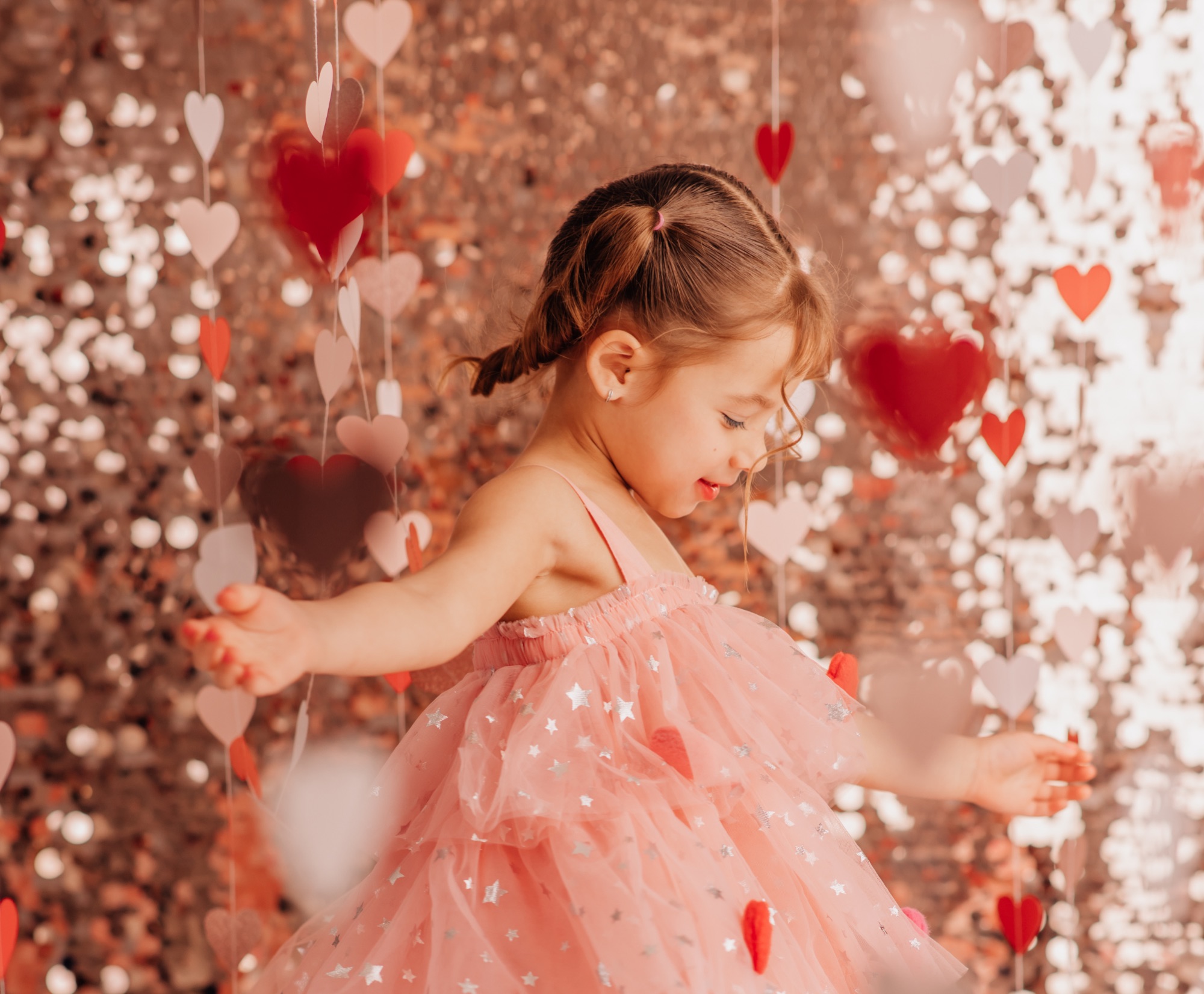 Little girl in a pink tulle dress twirling among hanging paper hearts at a Valentine mini session