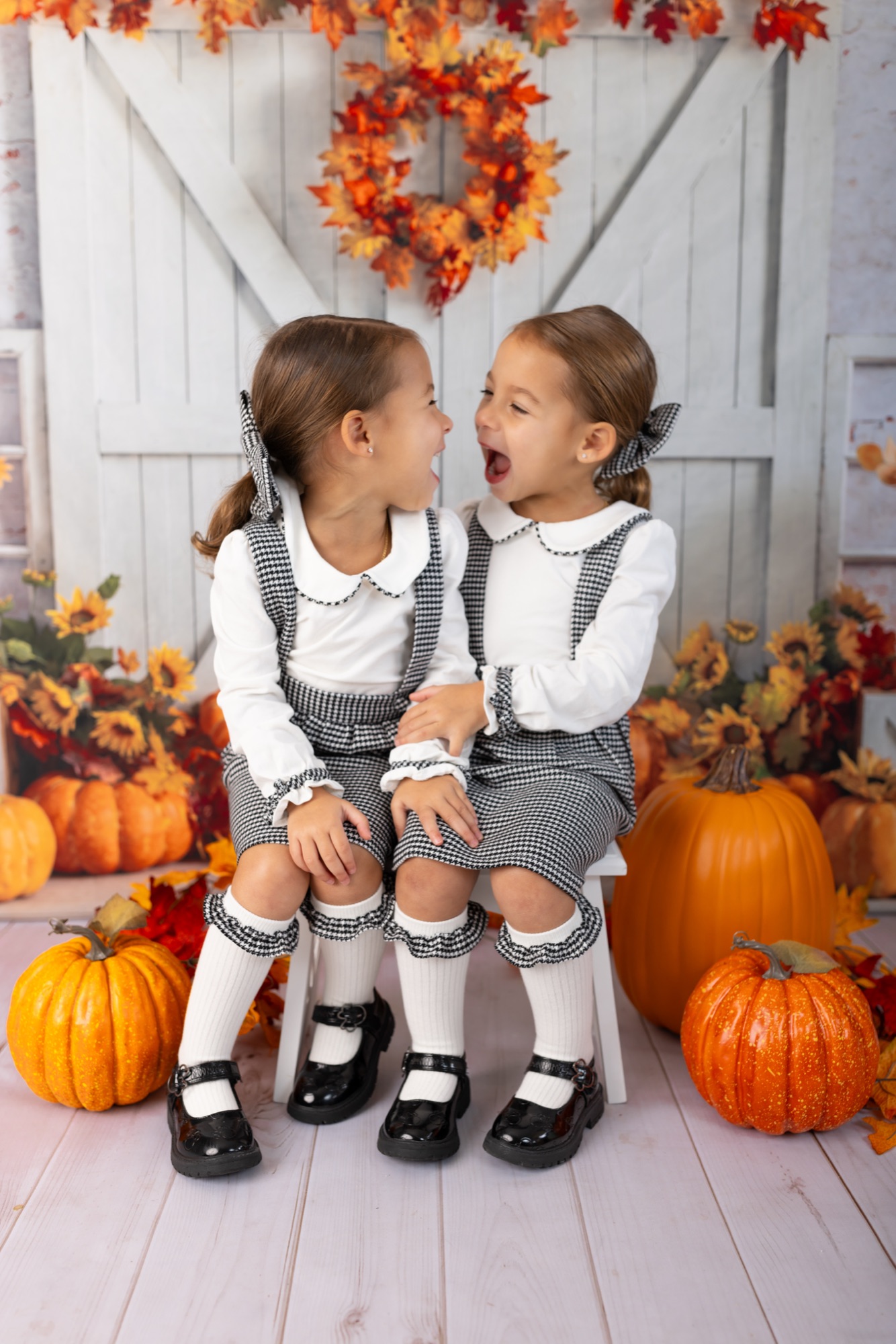 Two sisters laughing together on a fall mini session set with pumpkins and autumn leaves