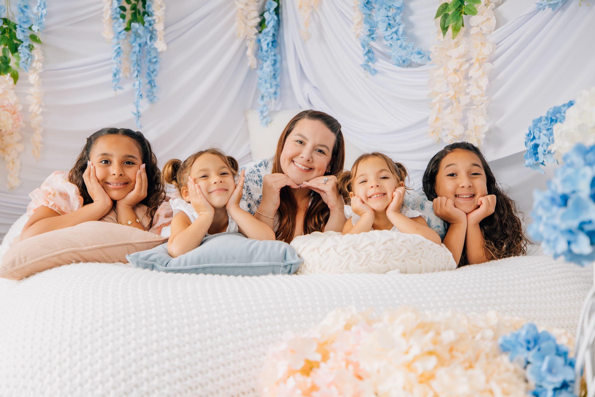 Marie and four little girls resting chin-in-hands on a flower-draped bed set at the studio