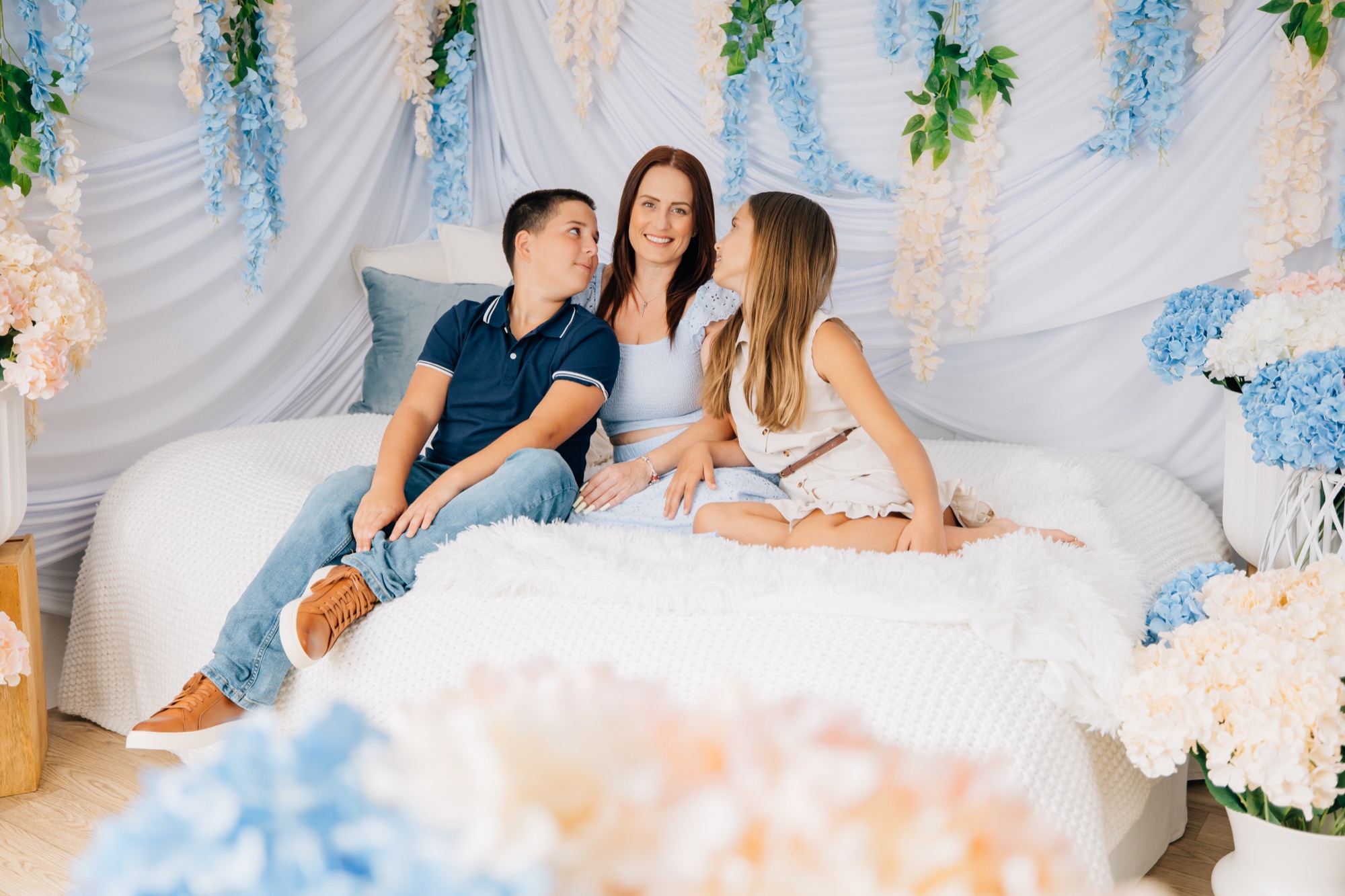 Mother with her son and daughter on a white bed set draped with blue and cream wisteria