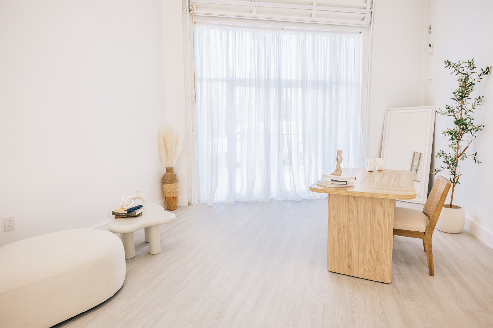 Sunlit studio corner with sheer curtains, standing mirror, and wooden desk